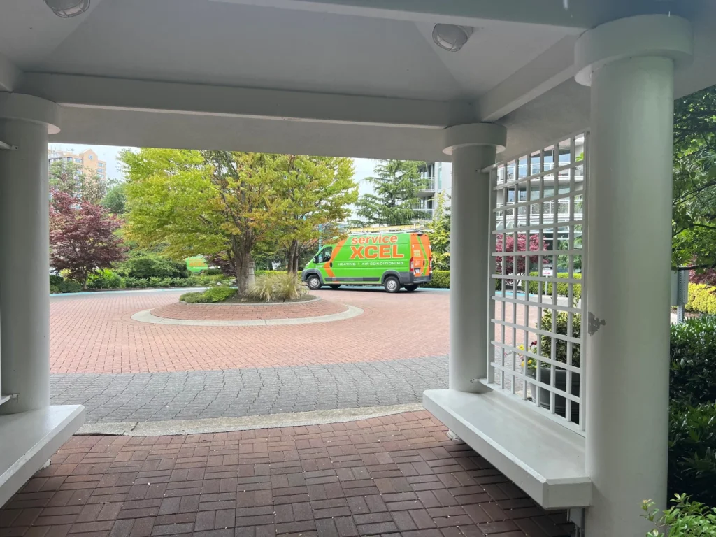 Green and orange Service Xcel heating and air conditioning van parked in a landscaped courtyard